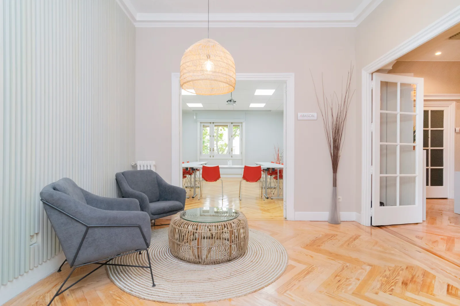 Sala de espera con parquet en espiga, sillones grises y acceso a sala de juntas