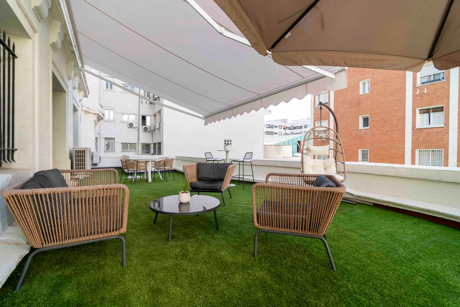 Terraza cubierta con sillones de mimbre y césped, ideal para reuniones informales