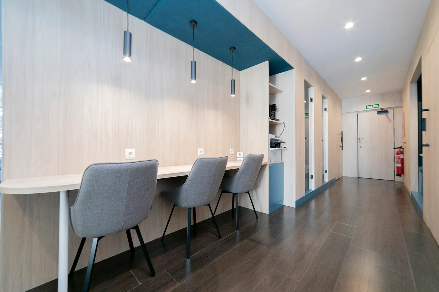 Sala de coworking con barra de trabajo, sillas tapizadas en gris y lámparas colgantes